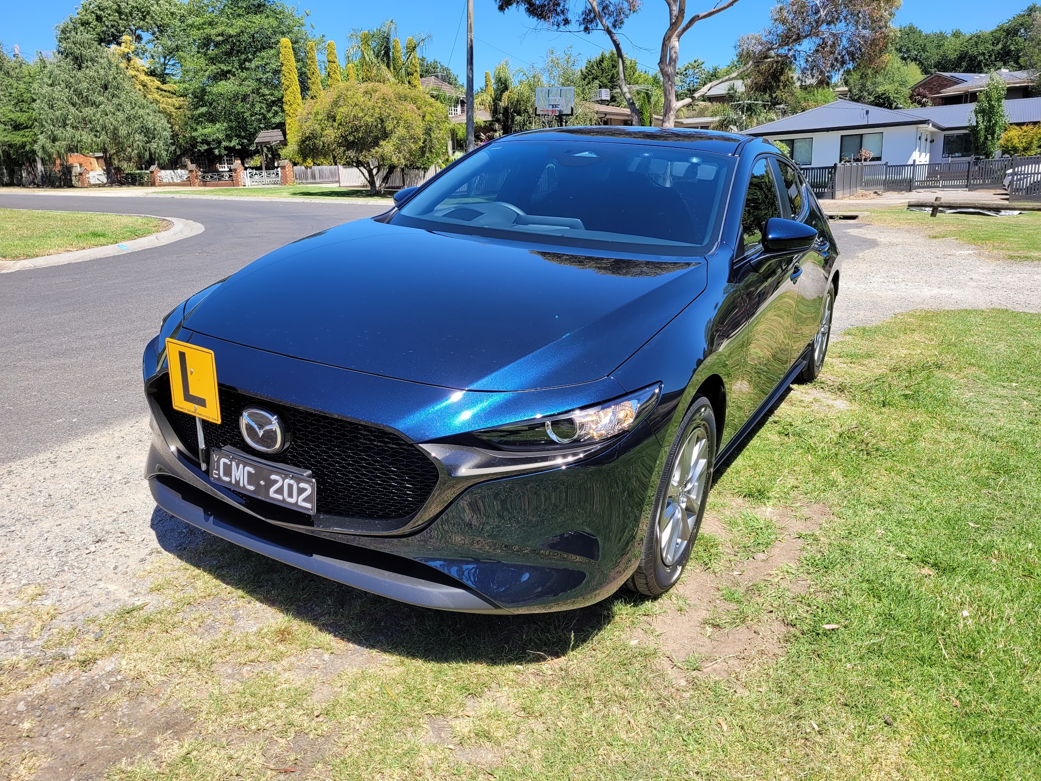 Front three-quarter view of the Bright Driver Academy Mazda 3 with its L-plate, parked on a grassy verge