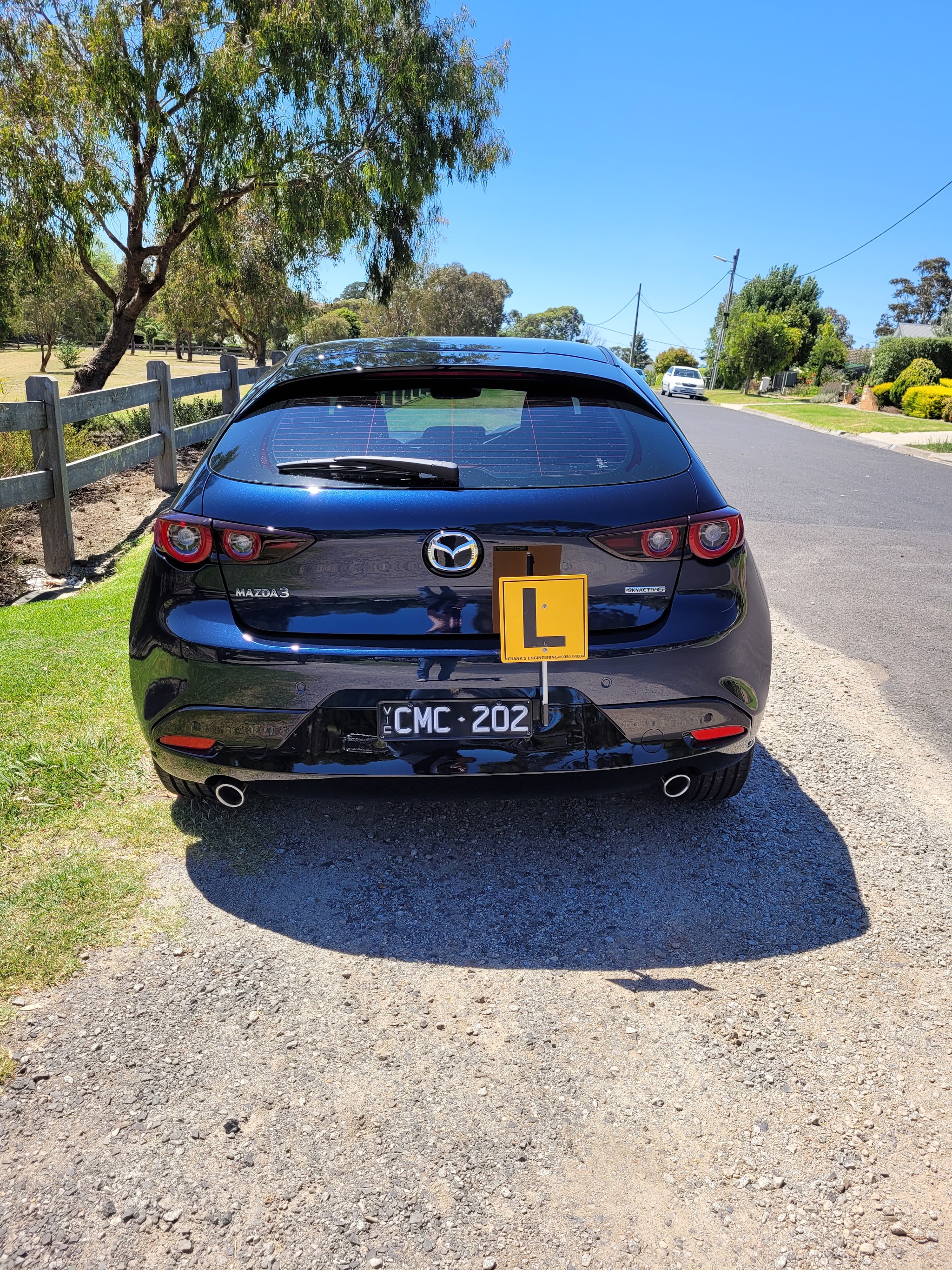 Rear view of the Bright Driver Academy Mazda 3 with its L-plate, on a quiet tree-lined road